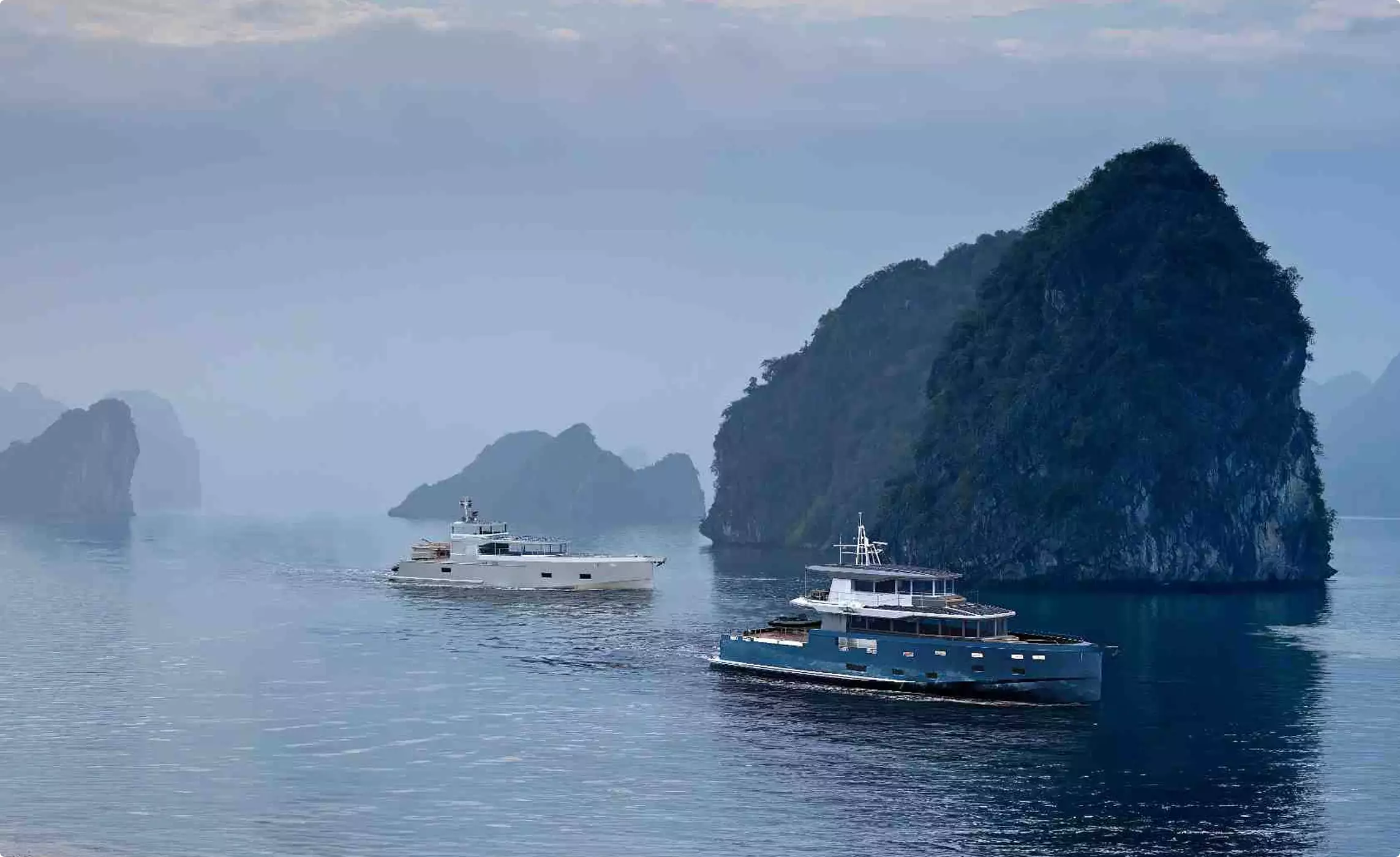 Boat rendering of two yachts cruising on calm water near misty limestone islands
