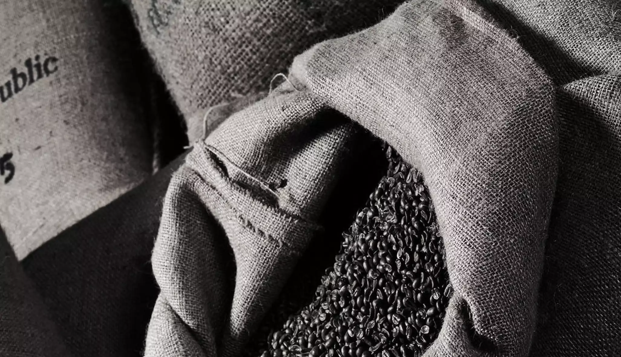 Open burlap sack spilling coffee beans as tactile espresso product design detail