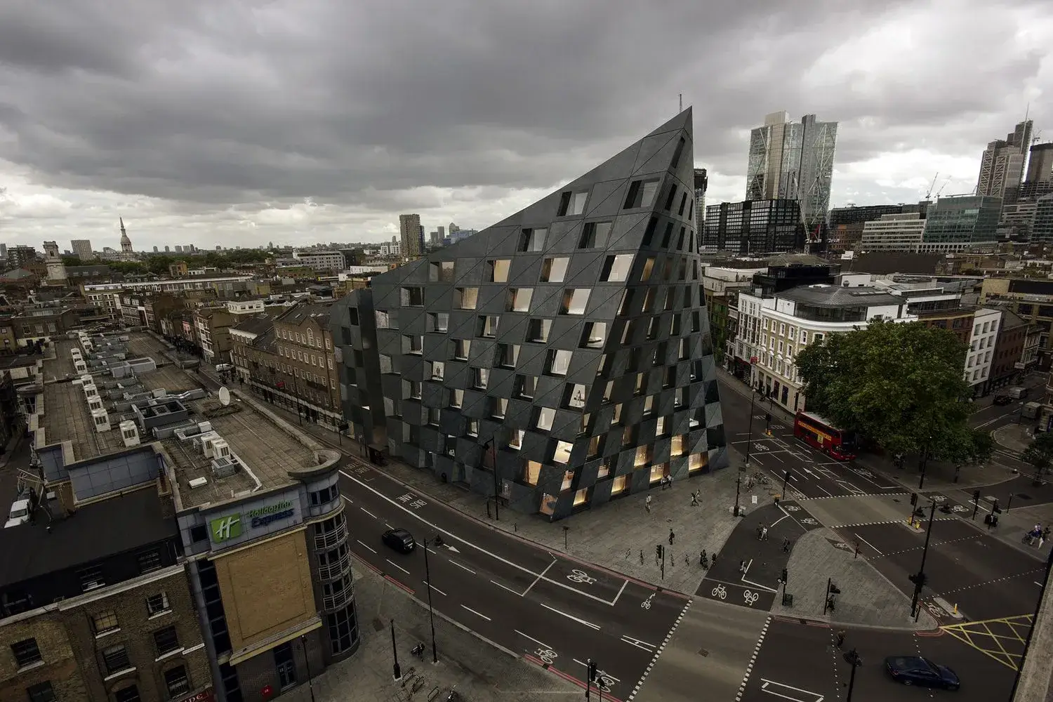 Contemporary architectural style building with angular facade at city street intersection under cloudy sky
