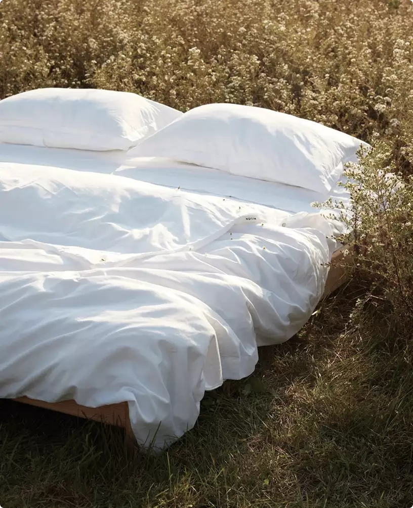 Minimalist outdoor bed with white bedding placed in wild grass field at golden hour furniture 3D rendering