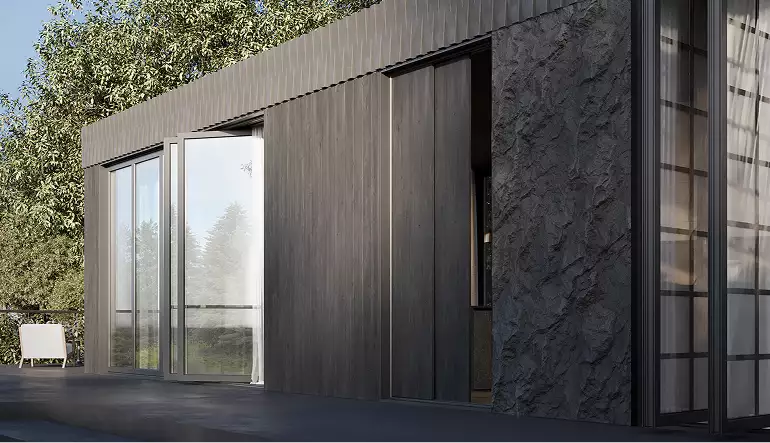 Modular home exterior side view with sliding panels, glass doors, and a textured dark wall
