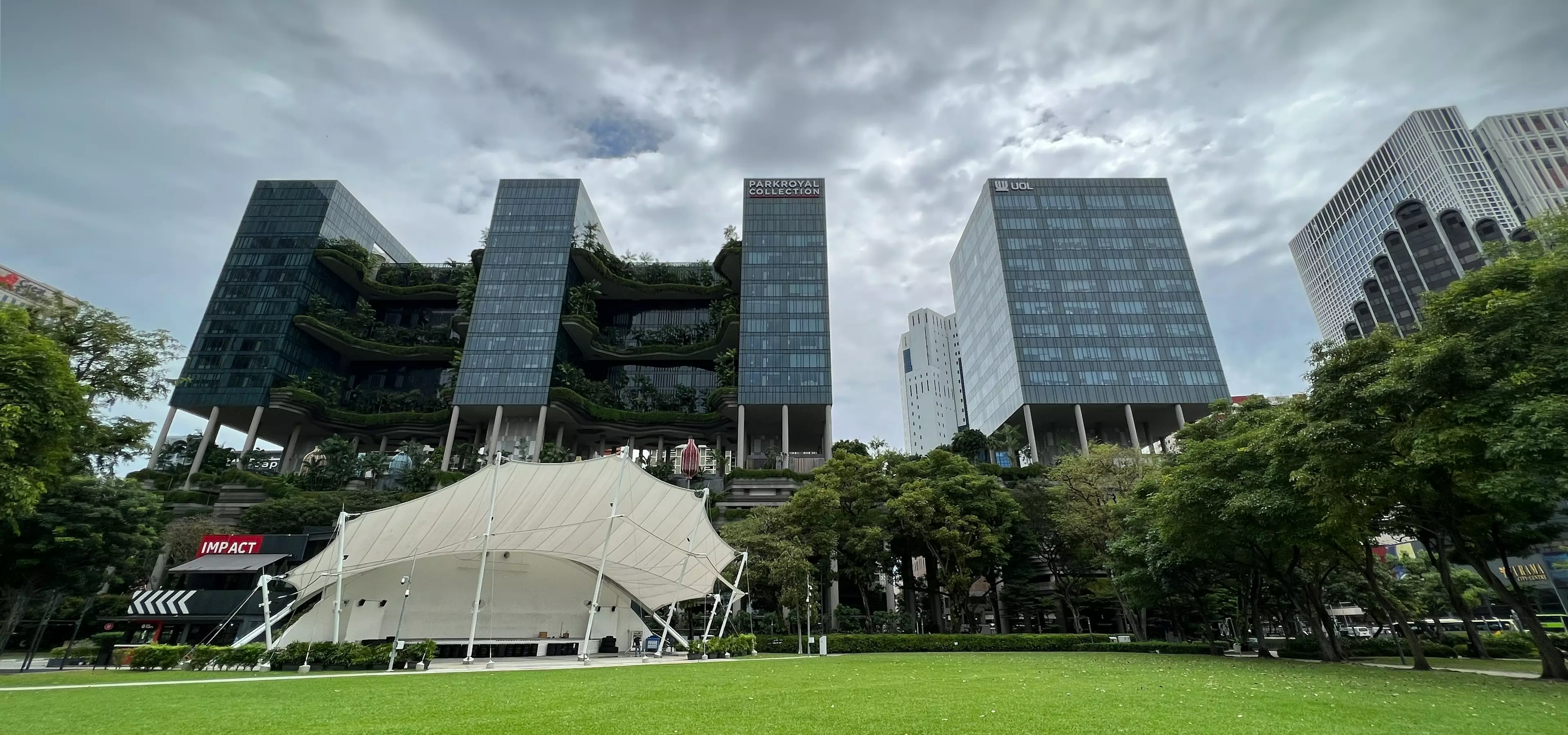 Urban green architecture towers with planted terraces, trees, lawn, and cloudy sky