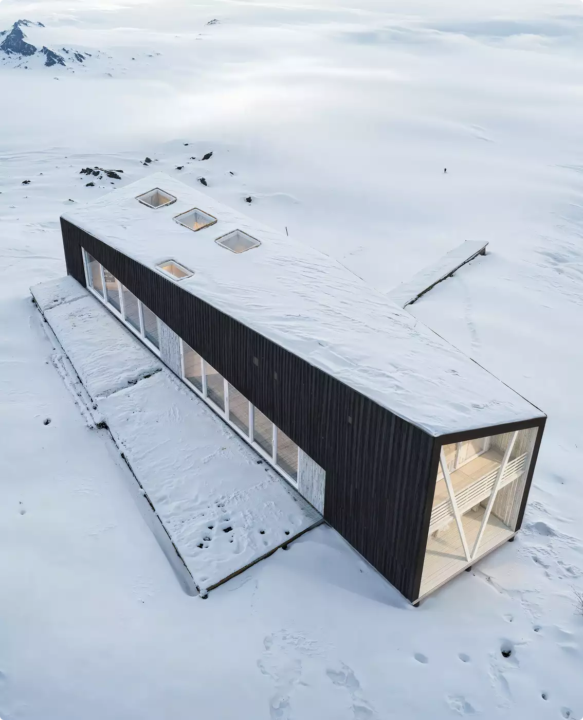 Realistic exterior winter renders of a long black cabin with skylights in a snow-covered landscape