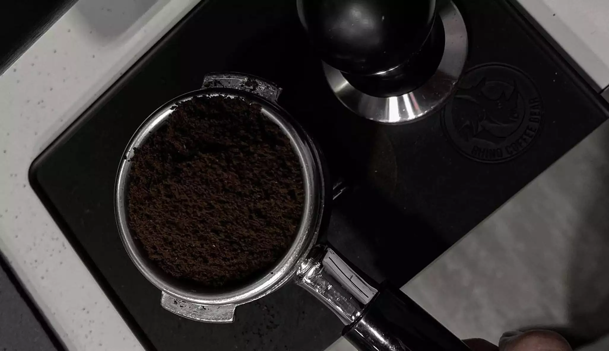Portafilter filled with tamped coffee grounds beside metal tamper in espresso product design scene