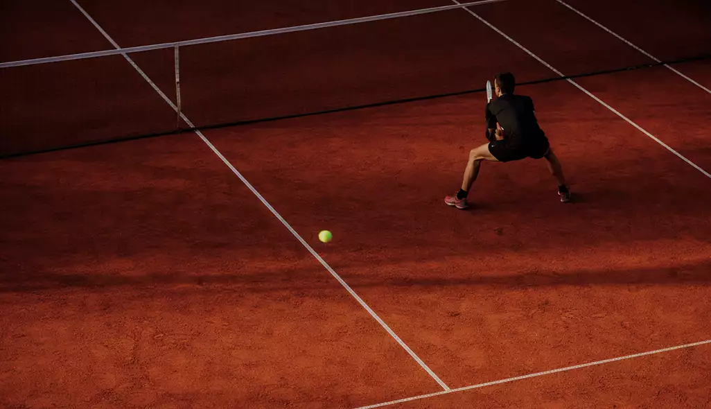 Tennis player on clay tennis court design preparing to return a shot, with clear white court lines visible