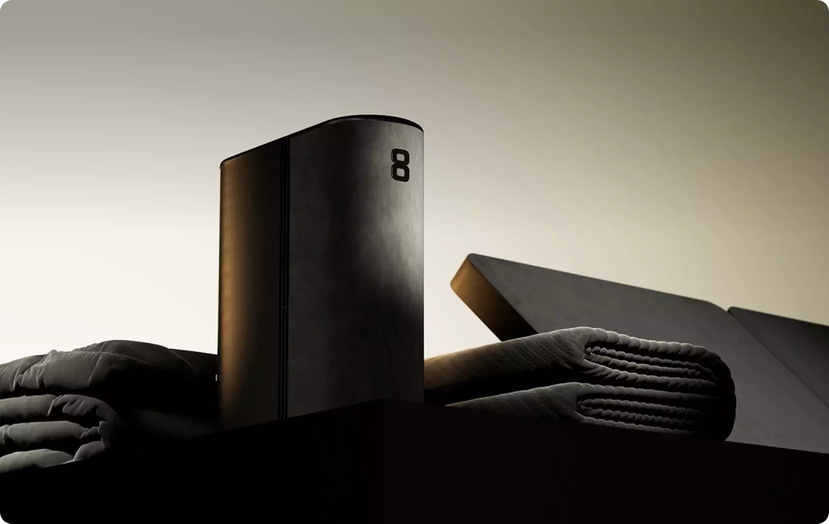 Hero shot sleek black rectangular device on bed with folded towels and open box