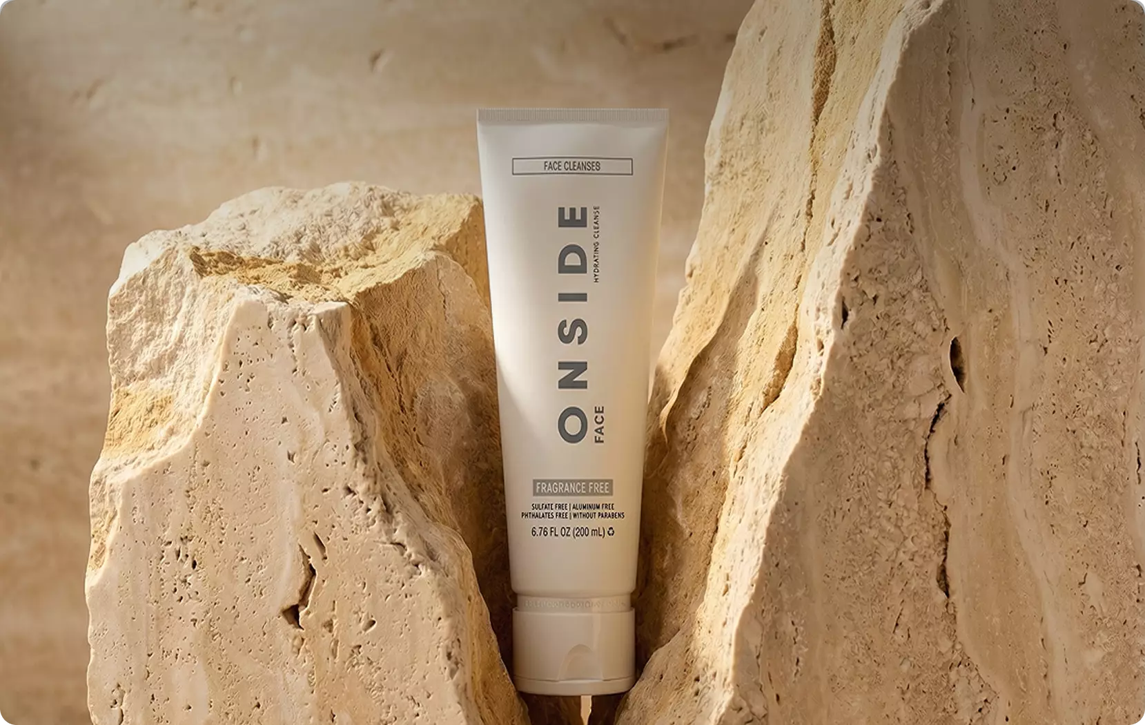 Lifestyle scenes face cleanser tube between beige rocks in warm natural setting