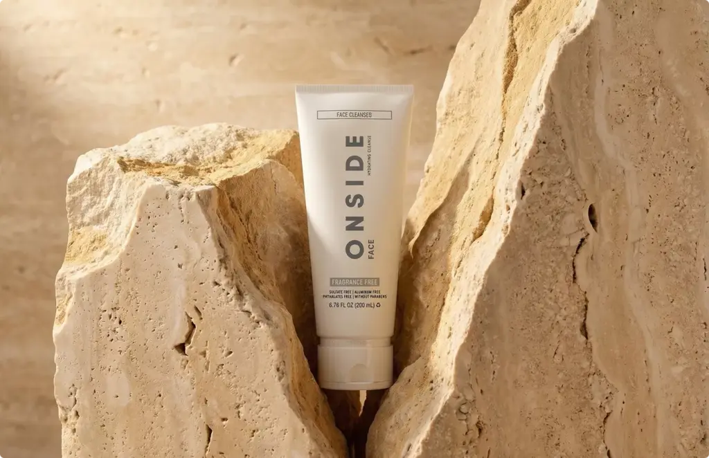 Skincare tube between textured stone blocks in studio, product rendering with warm natural tones
