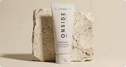 Skincare tube on textured stone blocks in neutral studio, product rendering with soft shadows