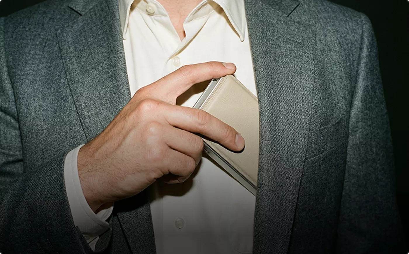 Hand placing slim wallet into jacket pocket, product rendering lifestyle detail shot