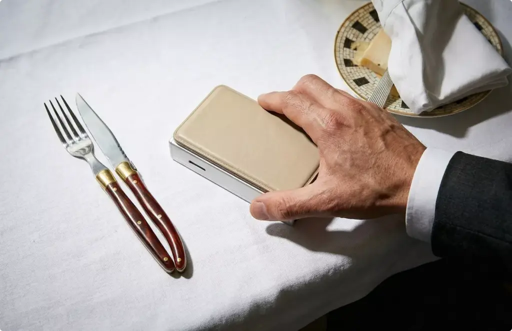 Hand holding slim wallet near table setting, product rendering lifestyle scene