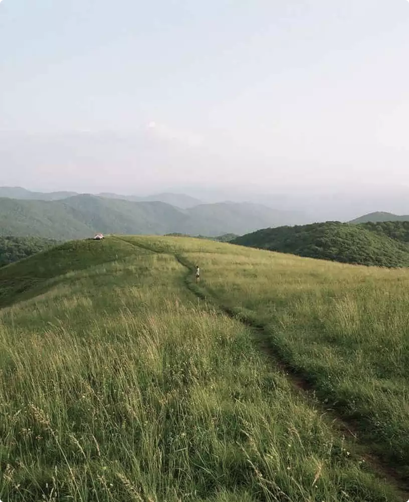 Retreat house design concept landscape with grassy ridge trail and layered mountains under hazy sky