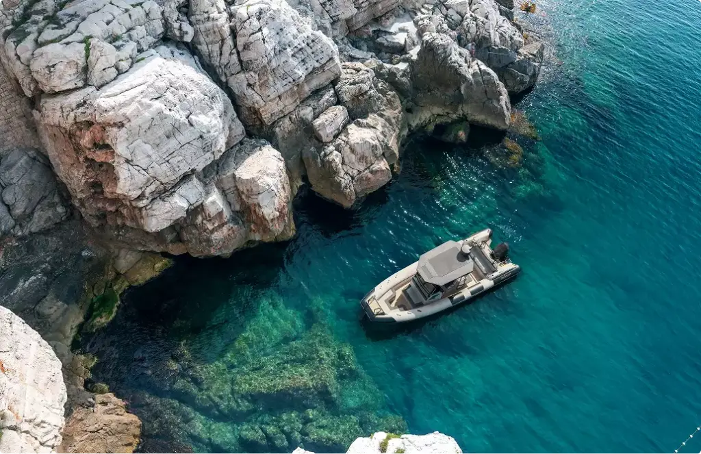 Aerial yacht rendering above rocky cove with clear water and boat near rugged shoreline