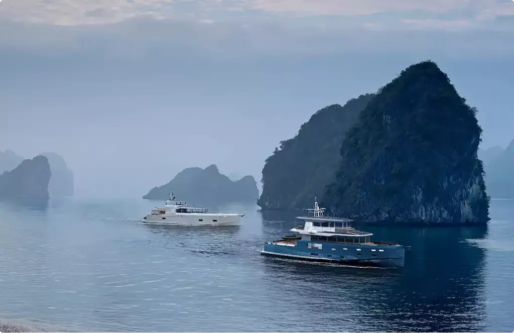 Two yacht rendering vessels on calm sea with misty islands and large rock formation nearby