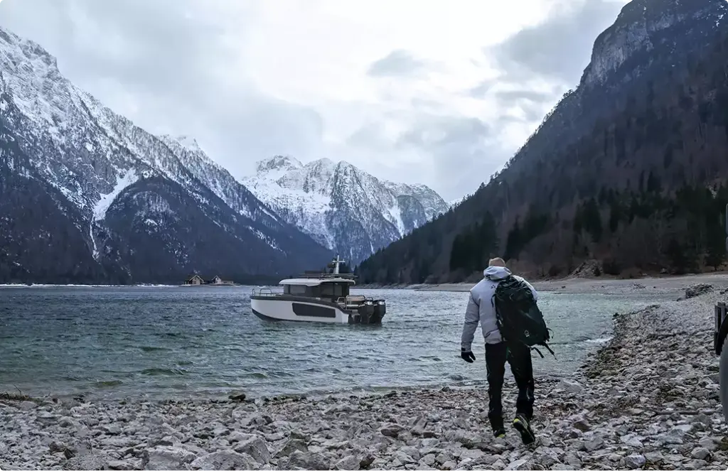 Explorer yacht rendering near rocky shore with person walking and snowy mountains behind