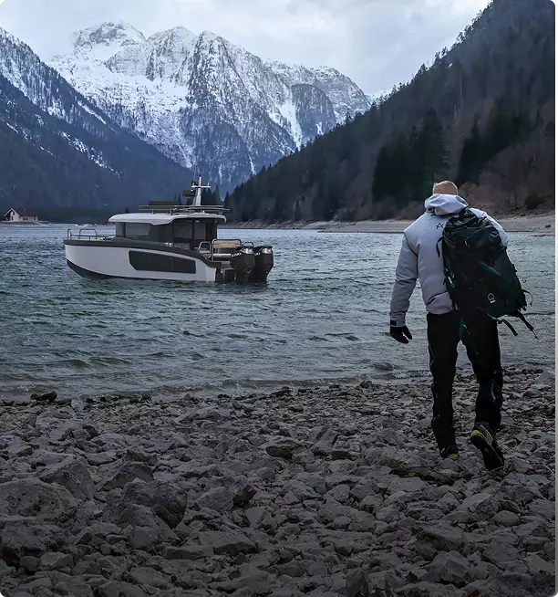 Explorer yacht rendering near rocky shore with person walking toward boat and snowy mountains