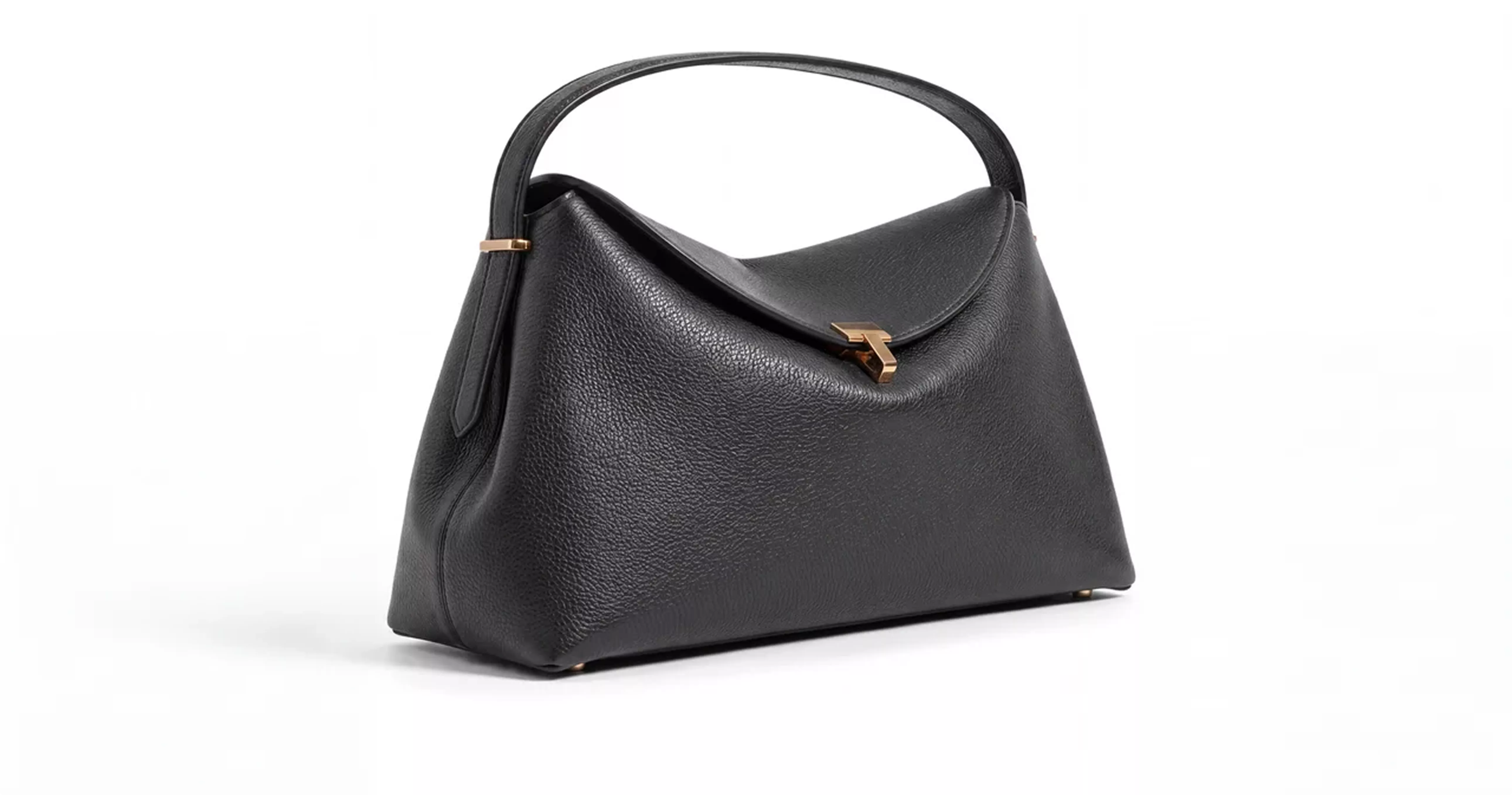 Black Toteme handbag with curved handle and gold clasp on gray background