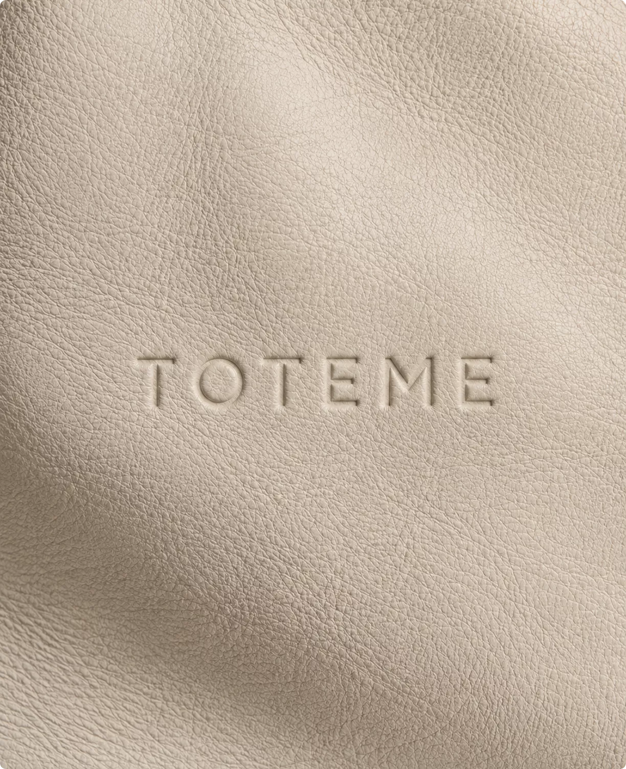 Embossed Toteme logo on beige textured leather surface