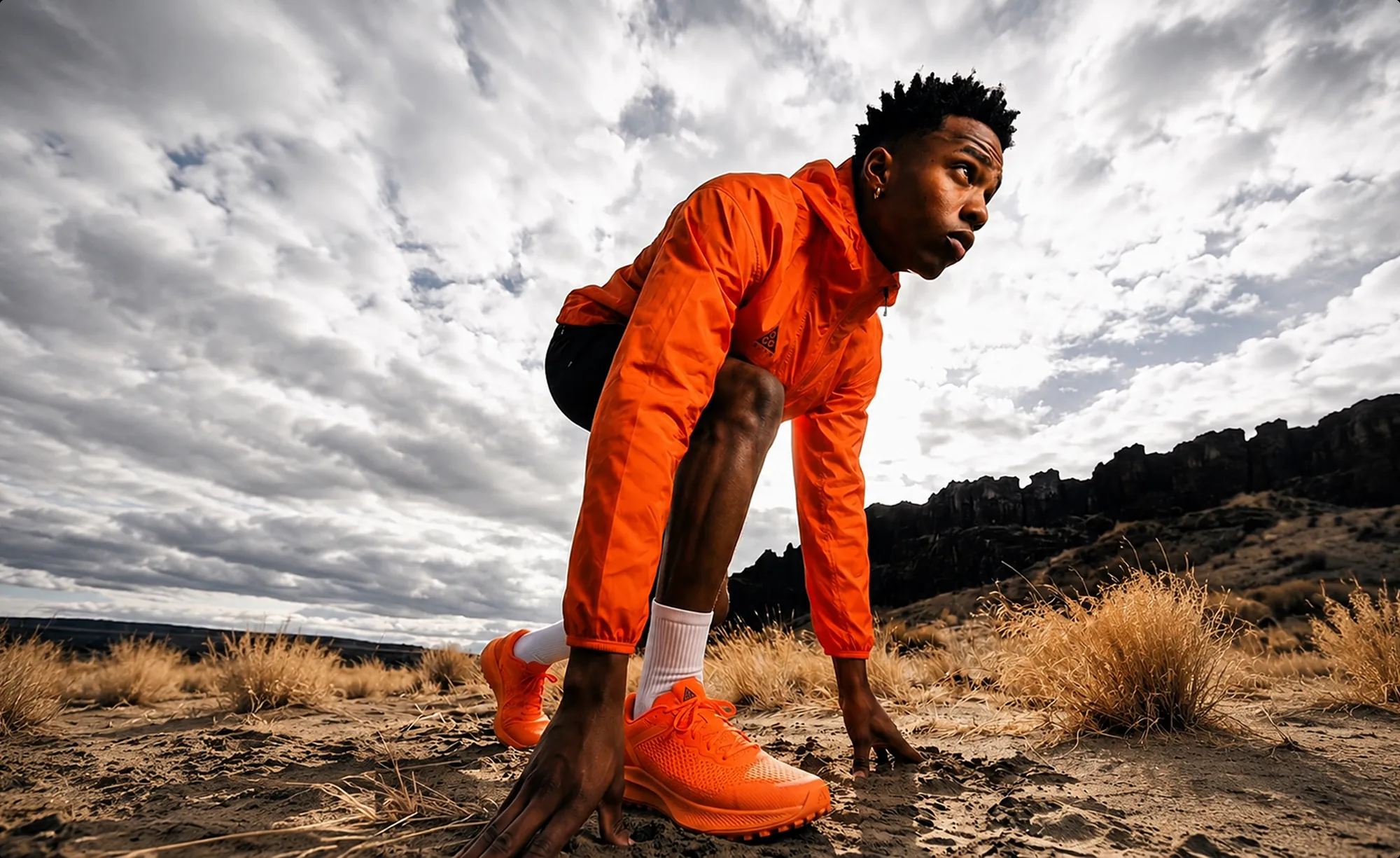 Athlete in orange in a starting crouch in a rocky landscape.